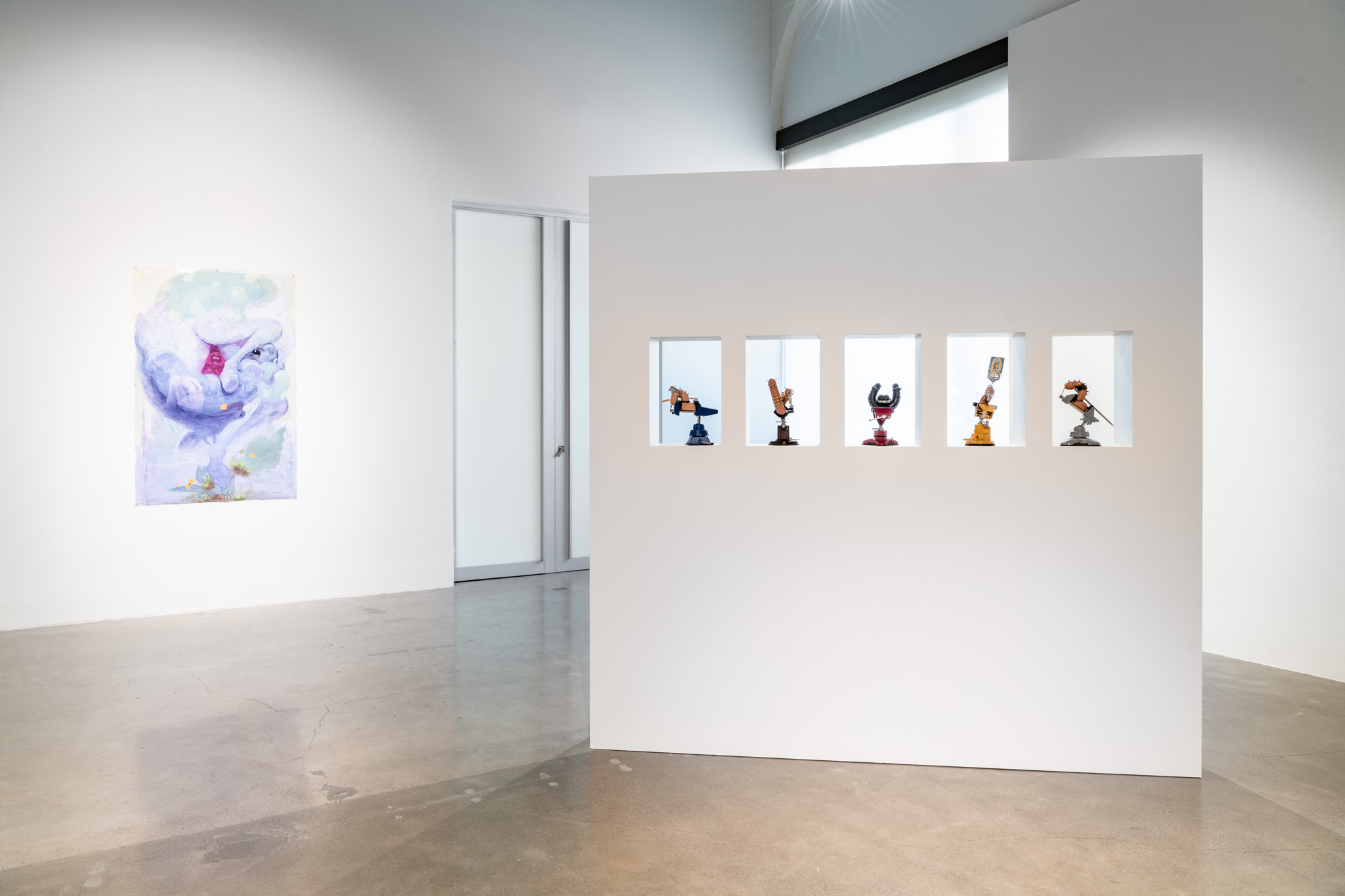gallery with white walls, vertical painting at back and small sculptures in cut-outs from standing wall