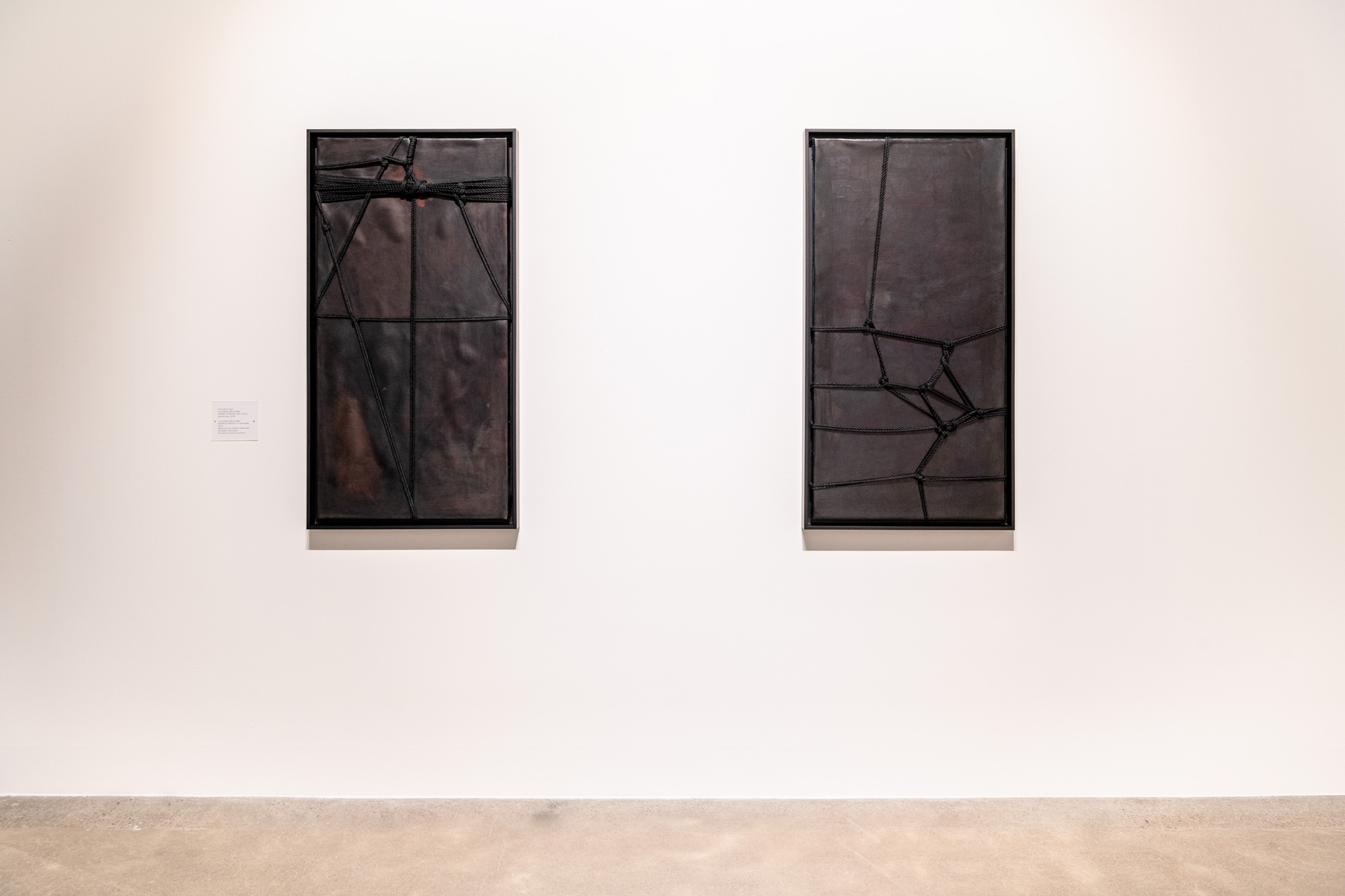 two vertical leather rectangles wrapped in black ropes and knots