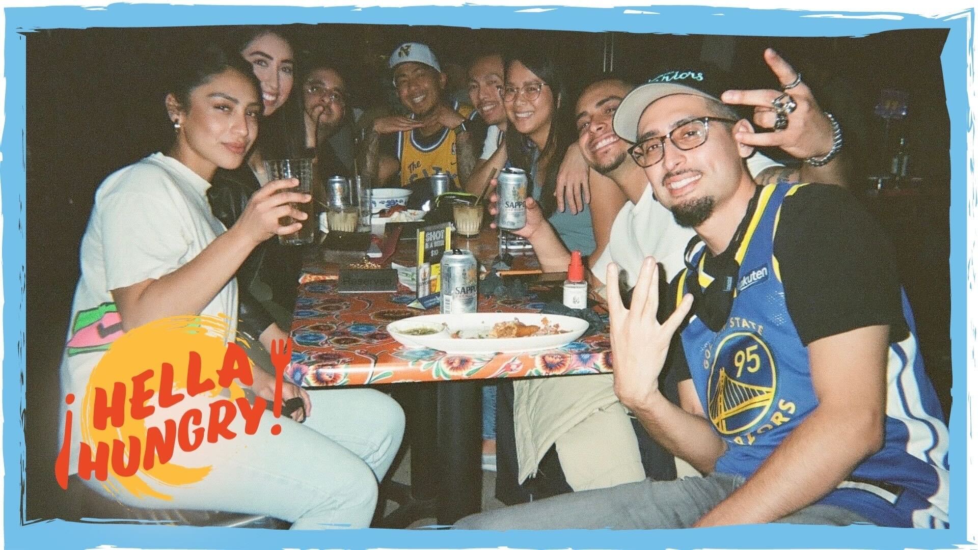 A group of friends pose for a photo while sitting at a table at a restaurant.