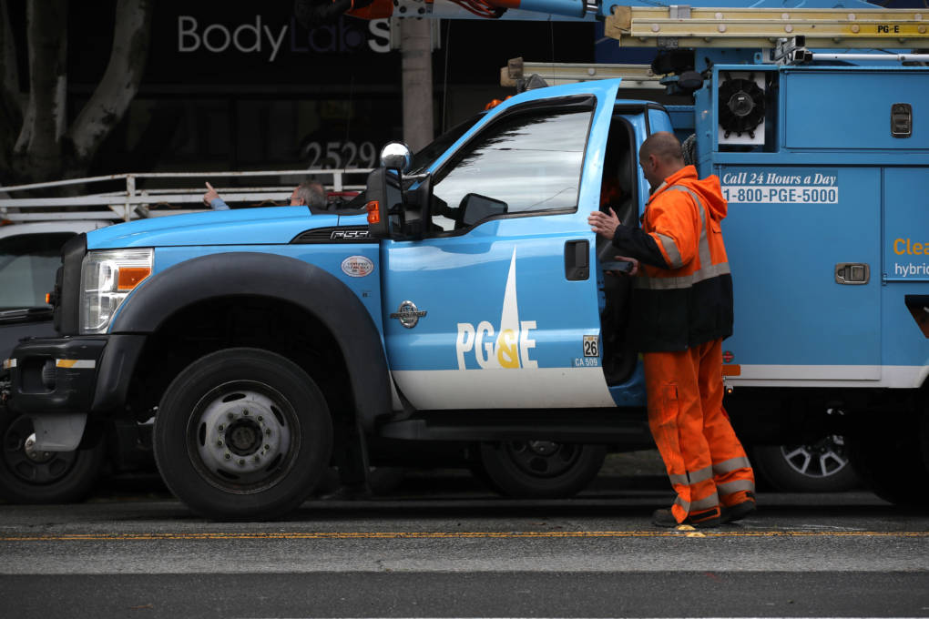A man dressed in bright orange safety gear opens the door of a blue truck that says "PG&E" on the side.