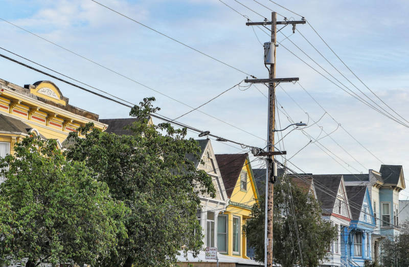 A photo of a telephone pole and its wires with different colored homes in the background.