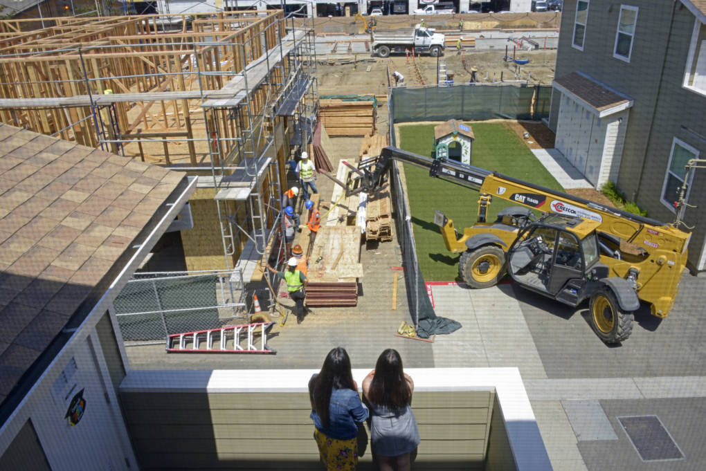 An overhead view of two women watching housing construction from their balcony.