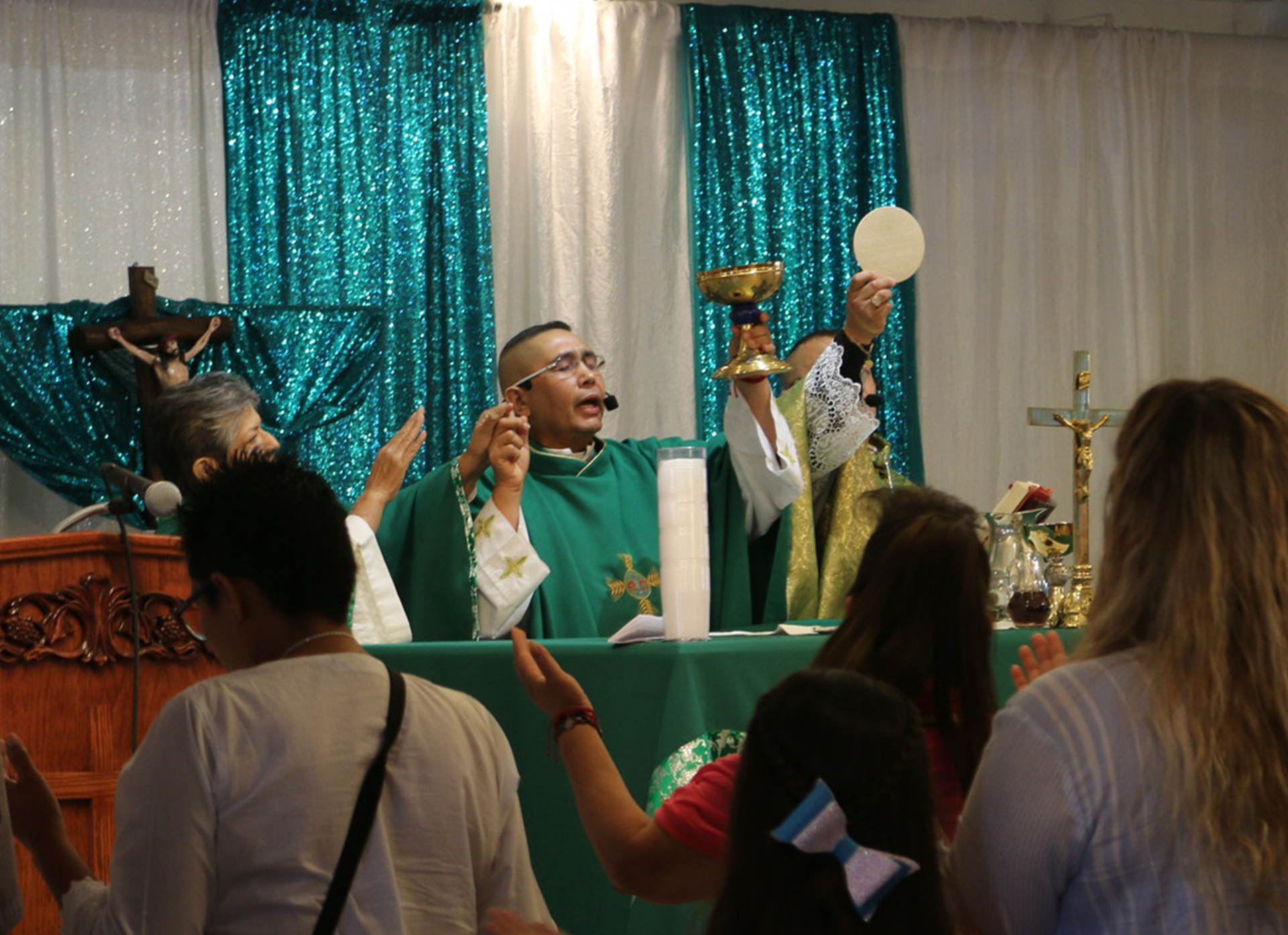 A priest in a green robe addresses parishioners.