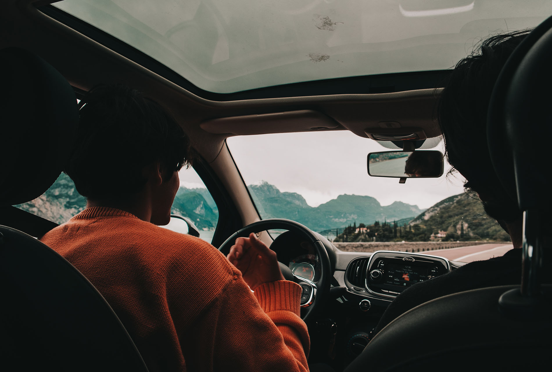 An image of a person driving a car in an orange sweater, taken from behind.