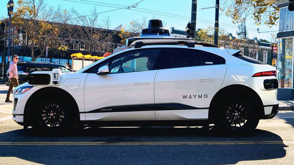 A white SUV with tech gadgets and cameras sticking out from the sides and roof waits at a stoplight in San Francisco's Castro neighborhood.