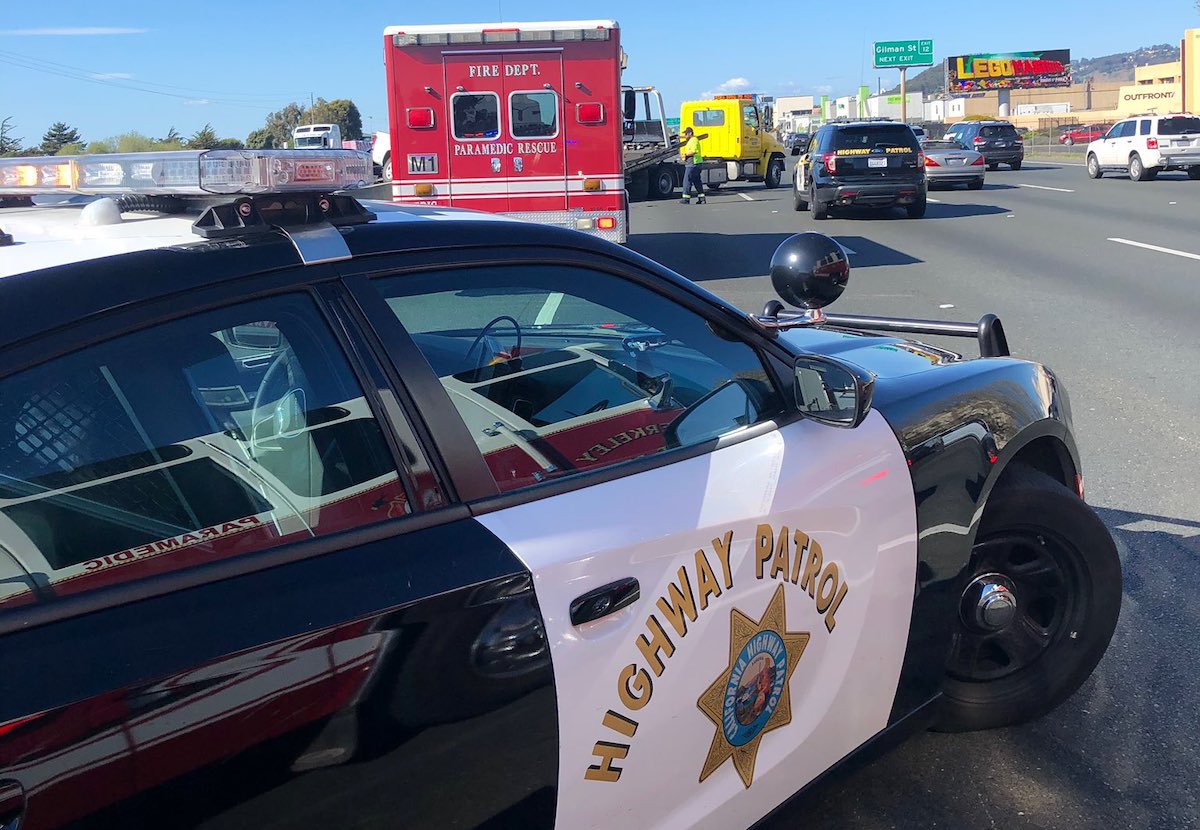 A car with black and white paint that reads "Highway Patrol" in gold letters is parked on the highway.