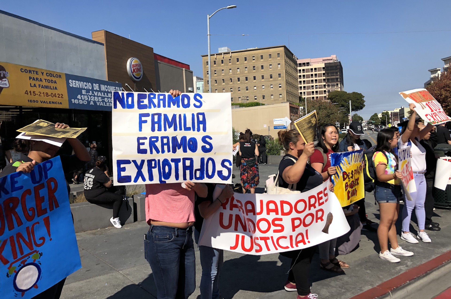 A group of people holding signs in Spanish, protesting in front of a Burger King restaurant.