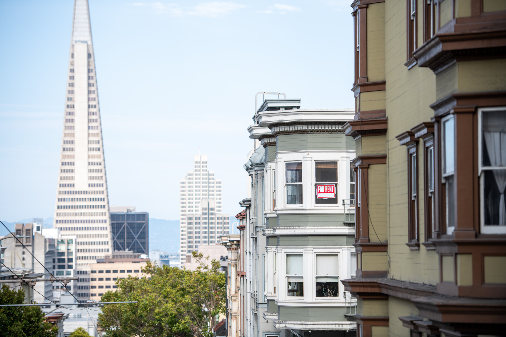 red sign hangs in window of classic SF victorian building with downtown skyline in background