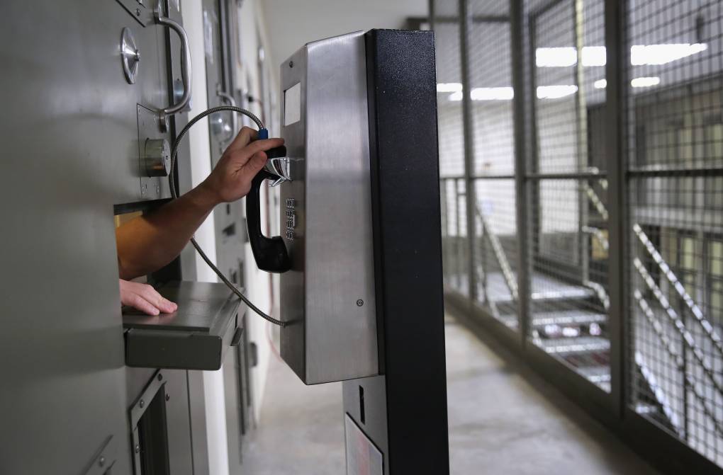 A hand reaches out from a cell to use a pay phone in a detention facility.