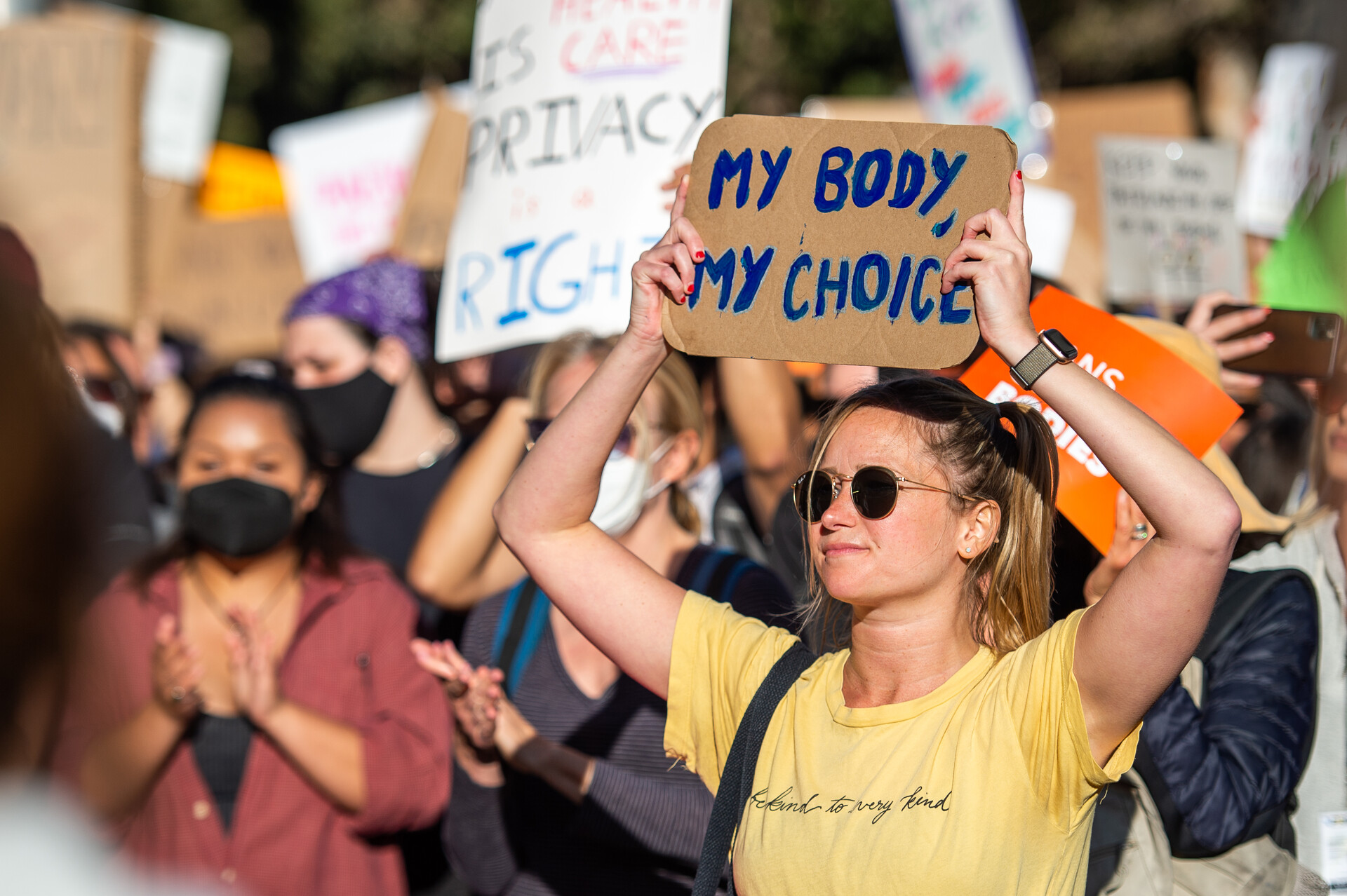 A crowd of people gather holding signs with messages like, "My body, my choice" written on them in colorful marker.