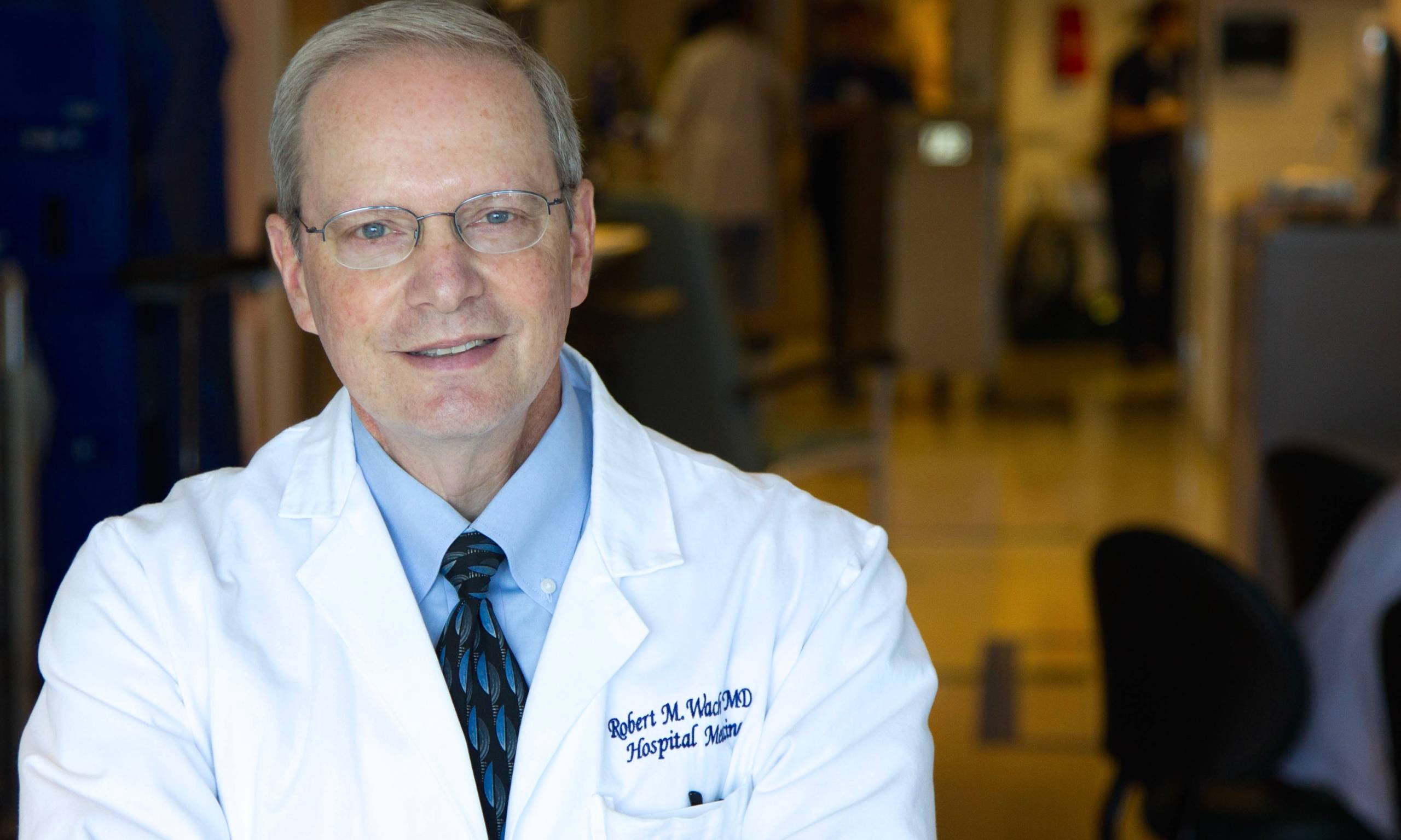 A man in his 60s with glasses and a doctor's frock smiles at the camera.