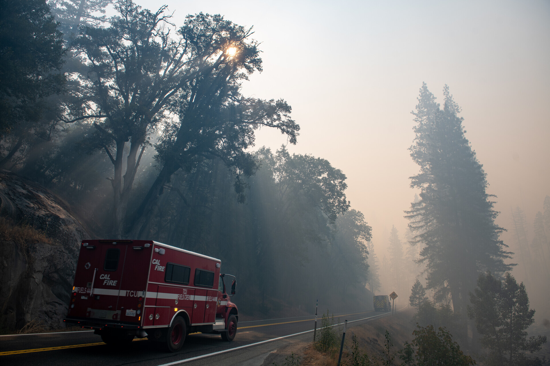 A smoke-filled view of woods with a fire truck on one side of the road.