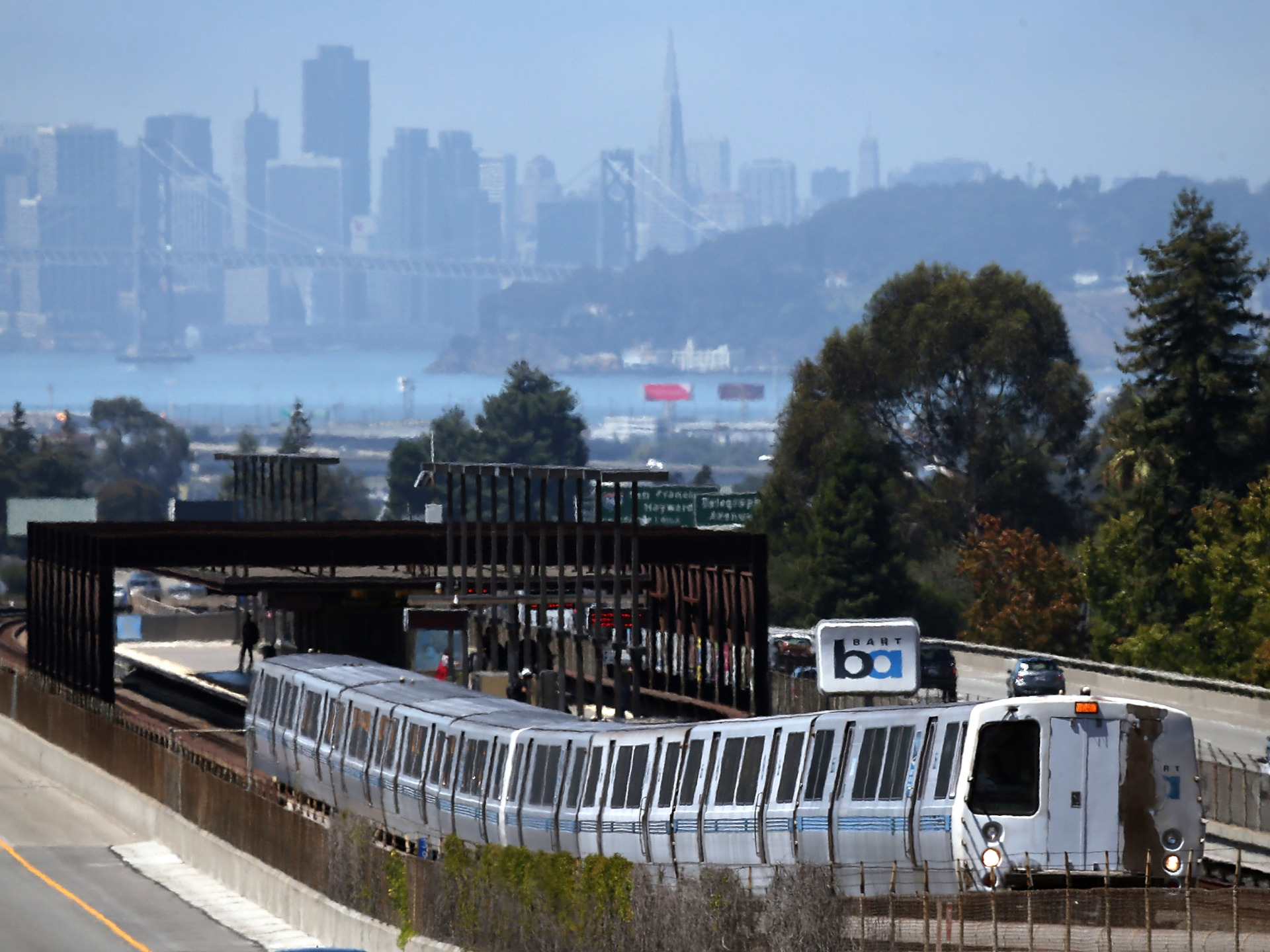 A BART train stops at an above ground station with San Francisco looming in the background