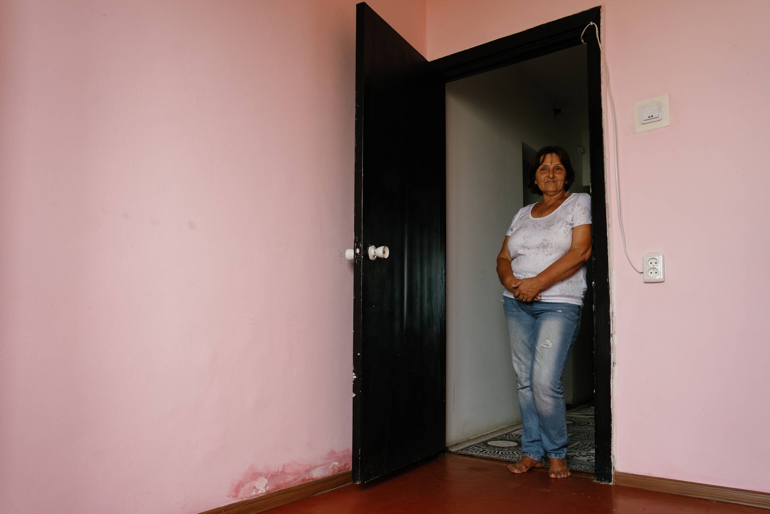 An elderly woman stands in the doorway of a pink room.