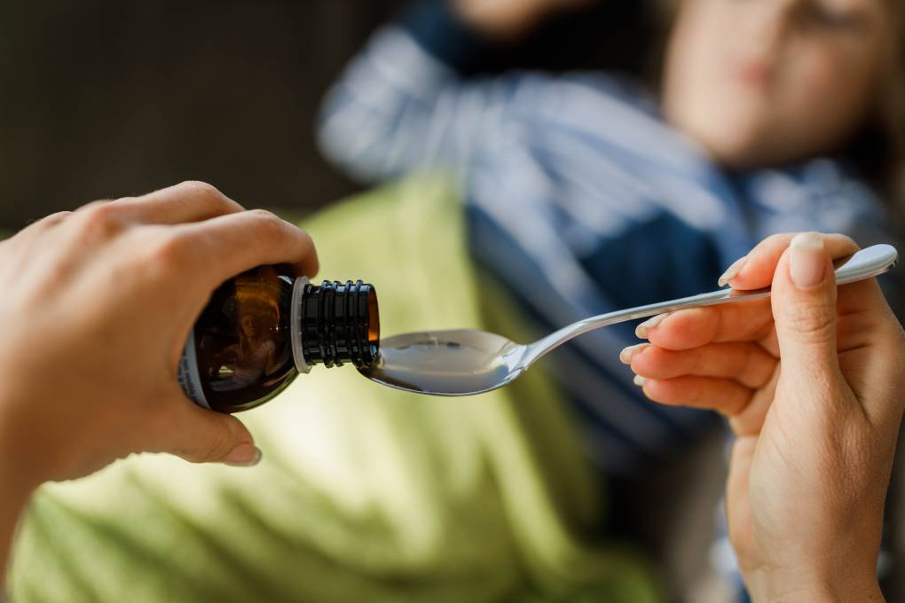 Close-up of an unrecognizable single mother pouring syrup into a spoon for her sick child.