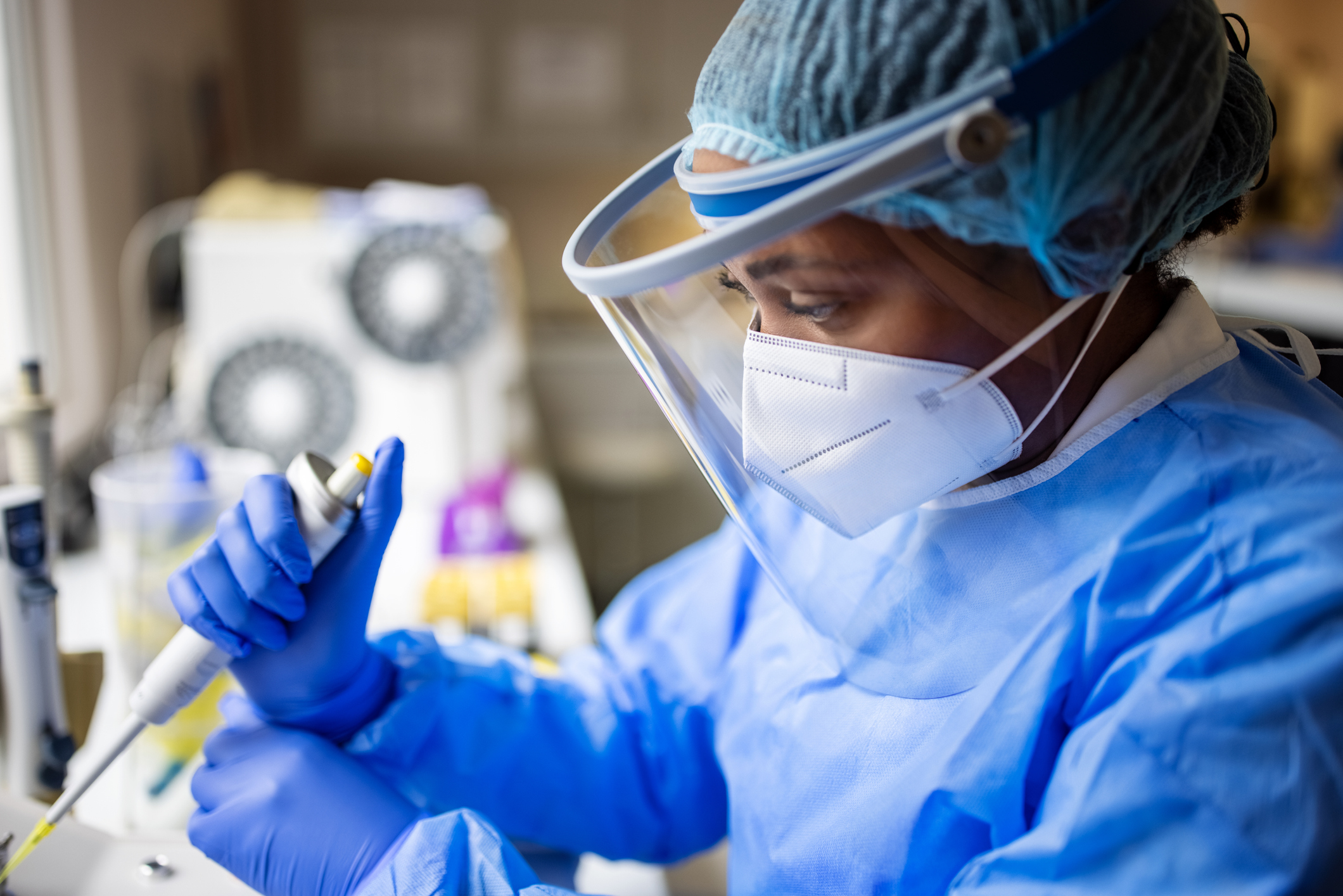 Female doctor wearing full PPE suit, face mask, and face shield working with pathogen samples in lab.