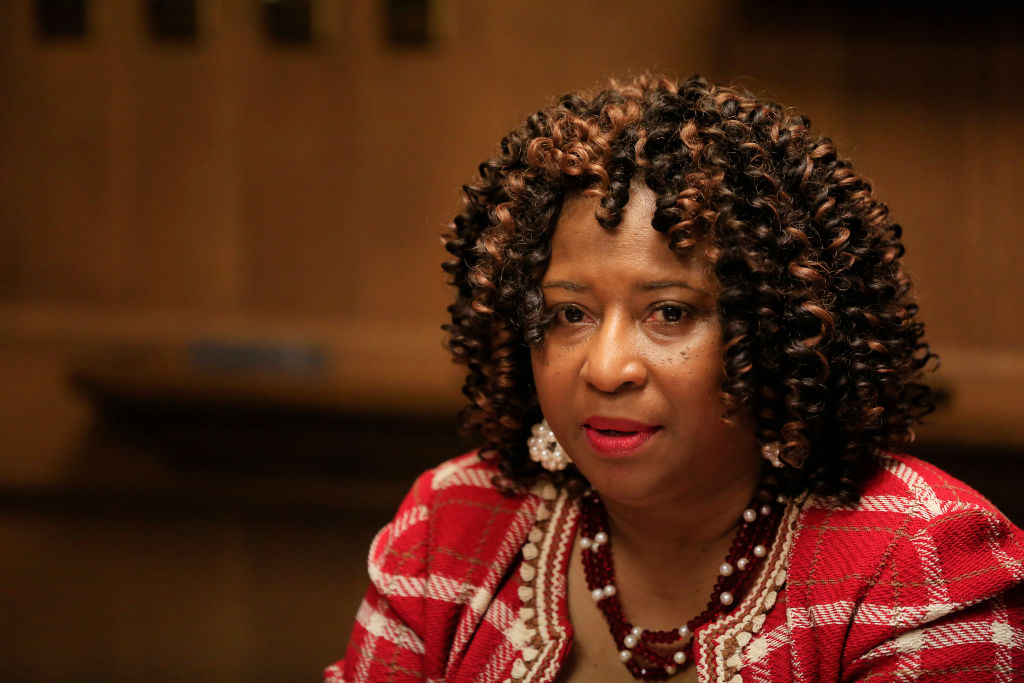 A Black woman looks at the camera, wearing a red dress and a necklace with shoulder-length hair.