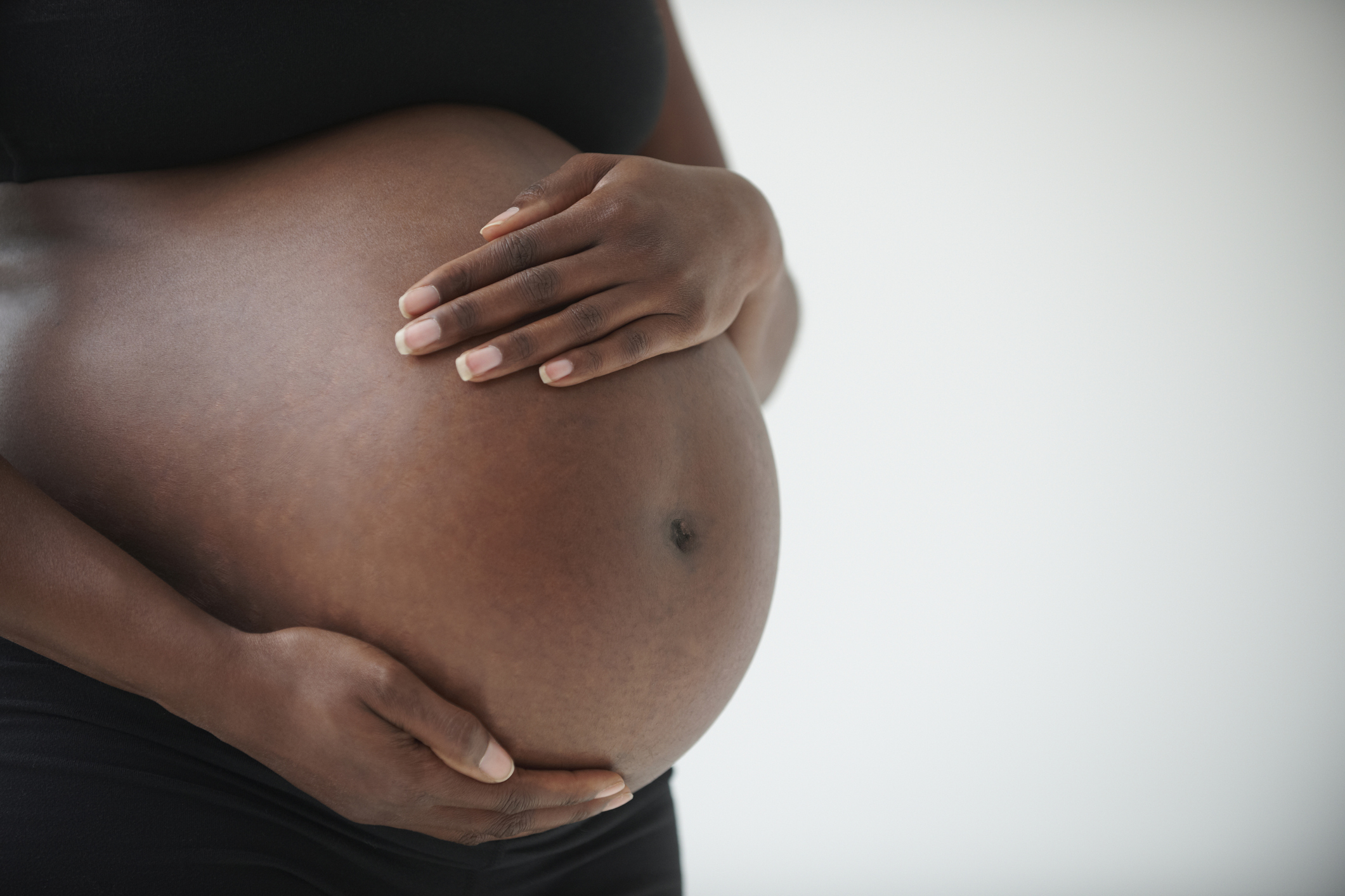 The midsection of a pregnant Black woman holding her belly.