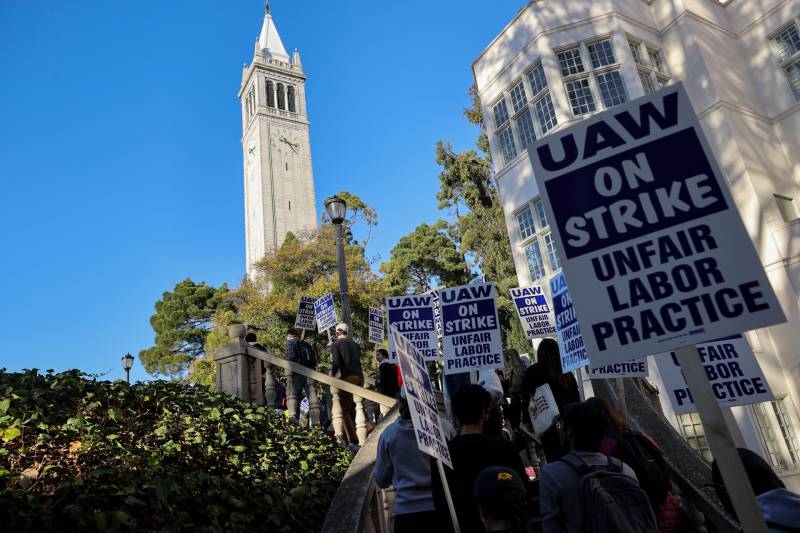 The UC Berkeley Campanile in the background as workers hold signs saying 'UAW on Strike'
