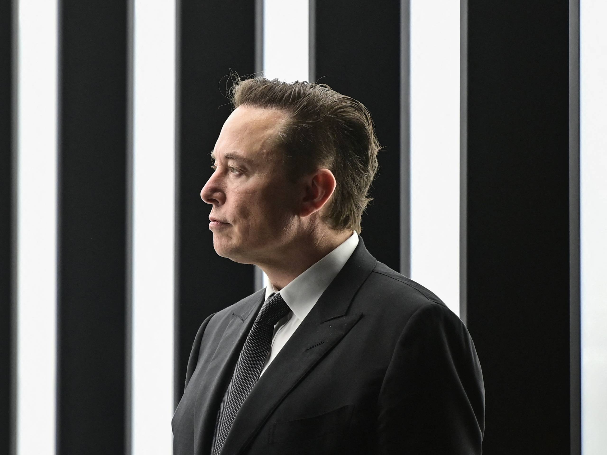 A man stands in a black business suit, looking to the left.