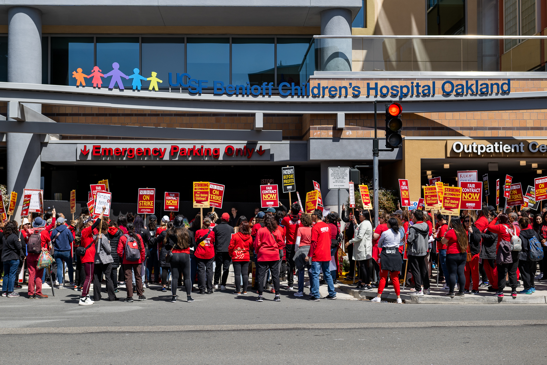 Hundreds of protesters in red T-shirts hold red and yellow picket signs outside of UCSF Benioff Children's Hospital Oakland.