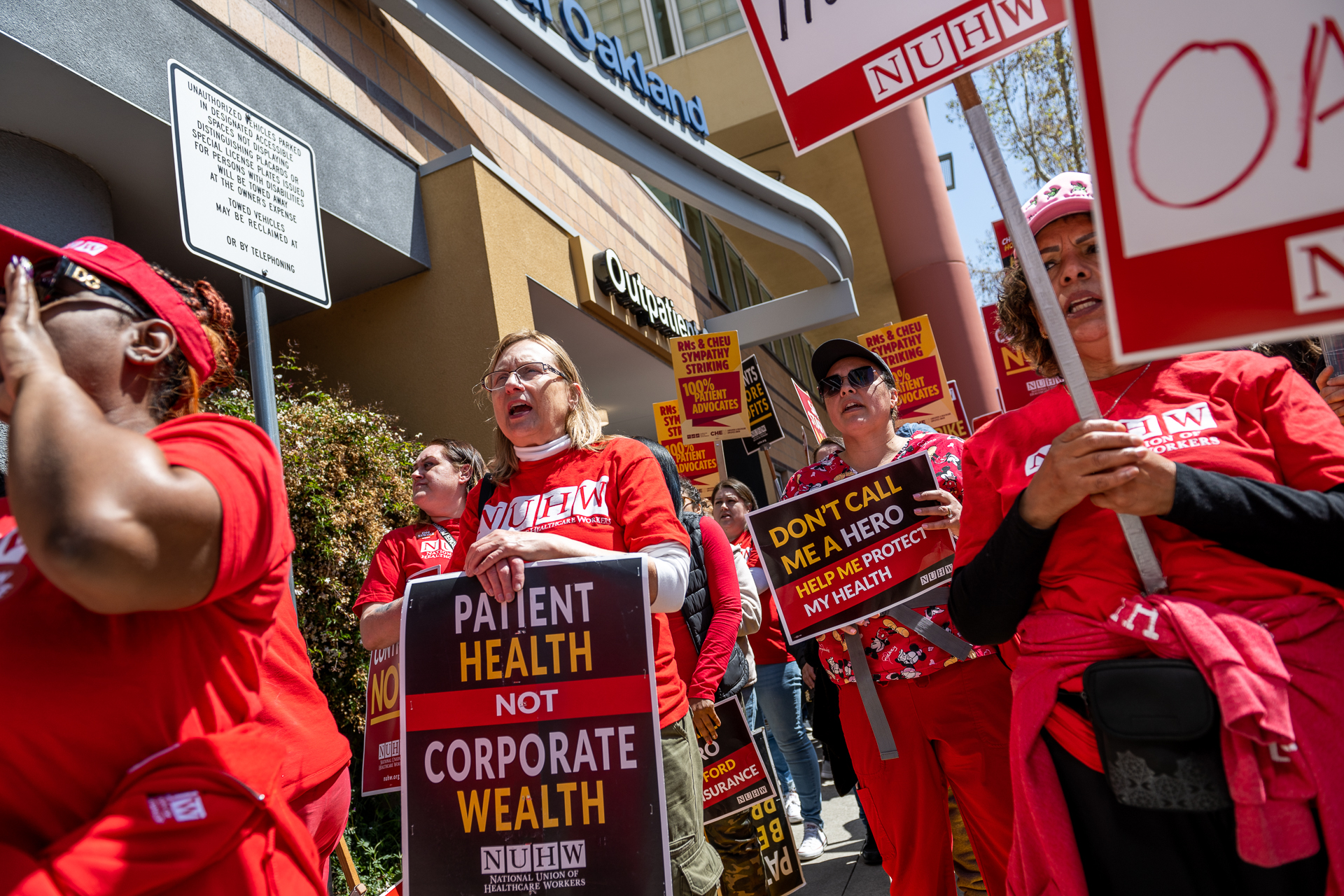 Hundreds of protesters in red T-shirts hold red and yellow picket signs outside of UCSF Benioff Children's Hospital Oakland.