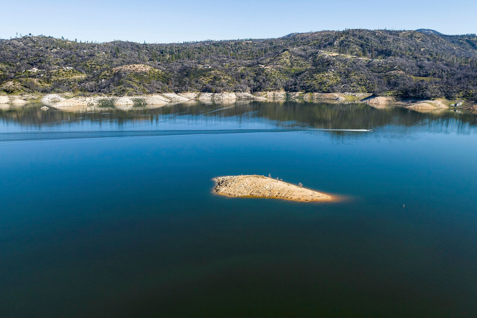 High view of a lake with mountains in the background. A small patch of land can be seen in the middle of the water.