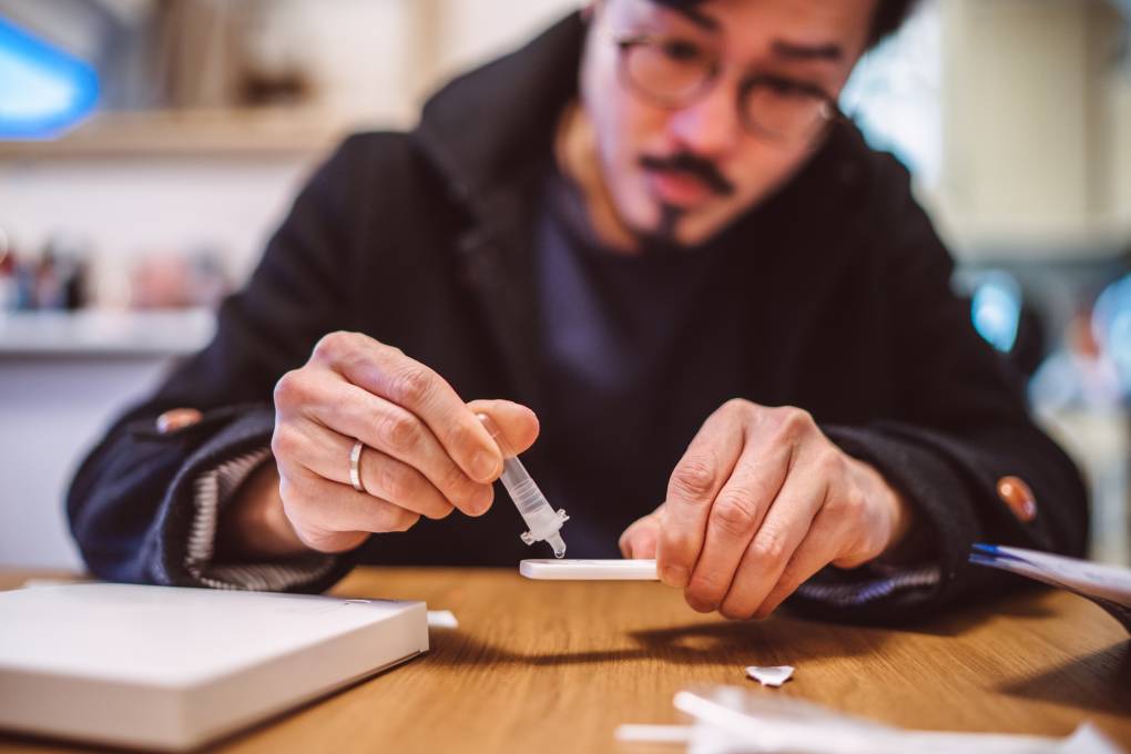 A man squeezes the sample liquid on a test strip while carrying out a COVID-19 rapid self test at home.