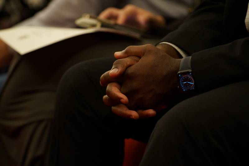 A close-up shot of a man's hands gently clasped together as he sits.