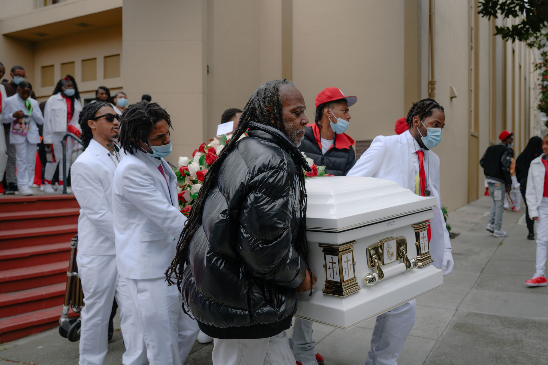 African American men carry a white coffin to a hearse outside a church.