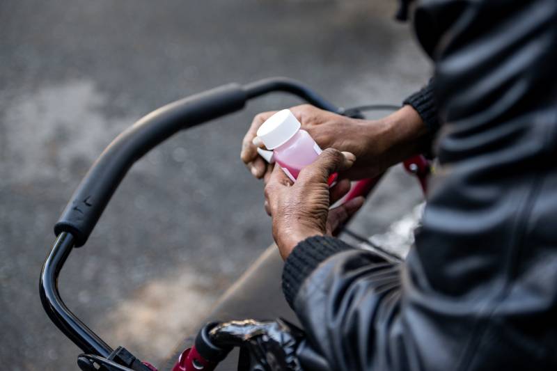 A woman leans on a walker while holding a clear prescription bottle with pink fluid inside.