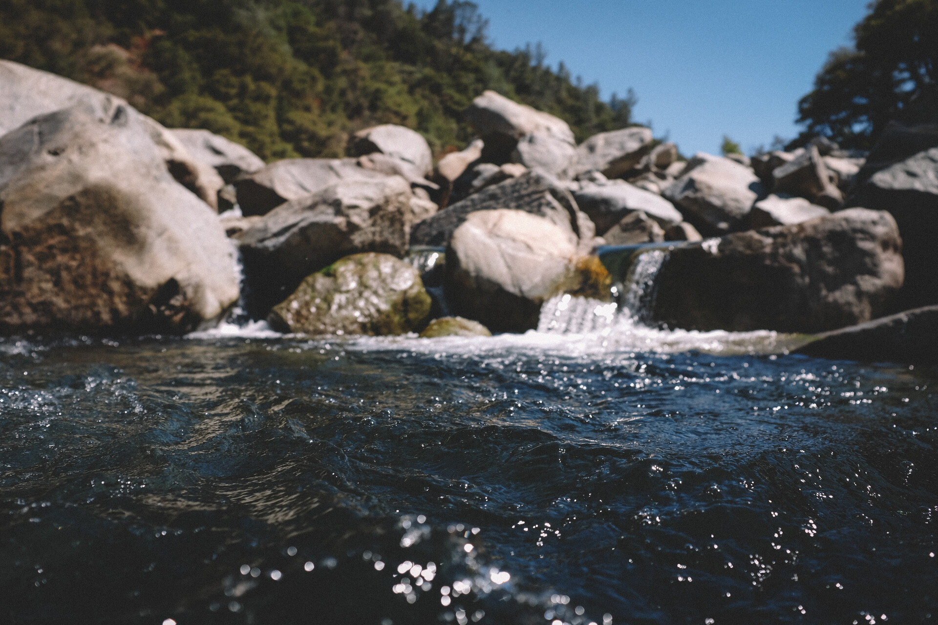A photo of the Yuba River taken from the water, showing a rocky outcrop of boulders at the water's edge.