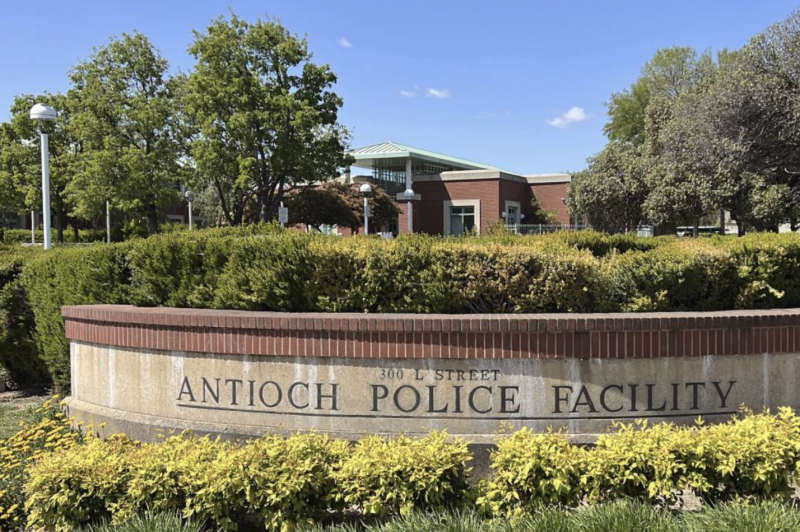 A sign carved into stone reads "Antioch Police Facility," with vegetation and a building in the background.