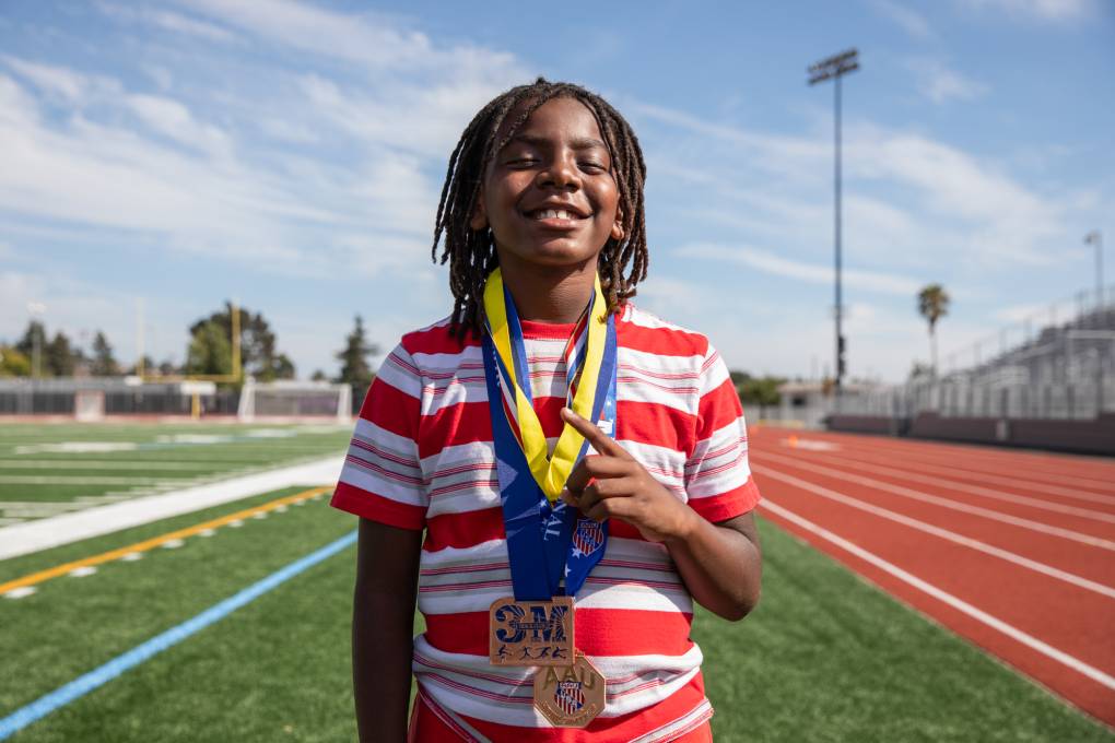 A boy poses for a photo with medals hanging from around his neck.