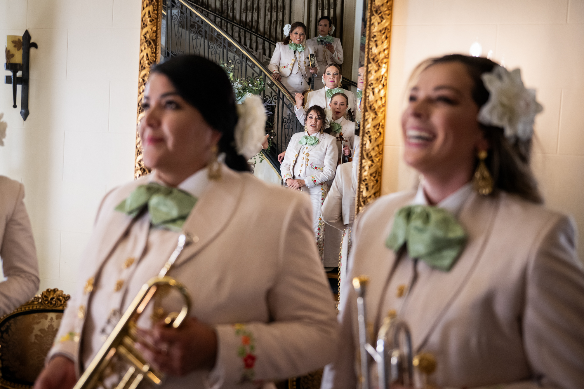 Women wearing ornate white outfits and holding instruments in an indoor setting.