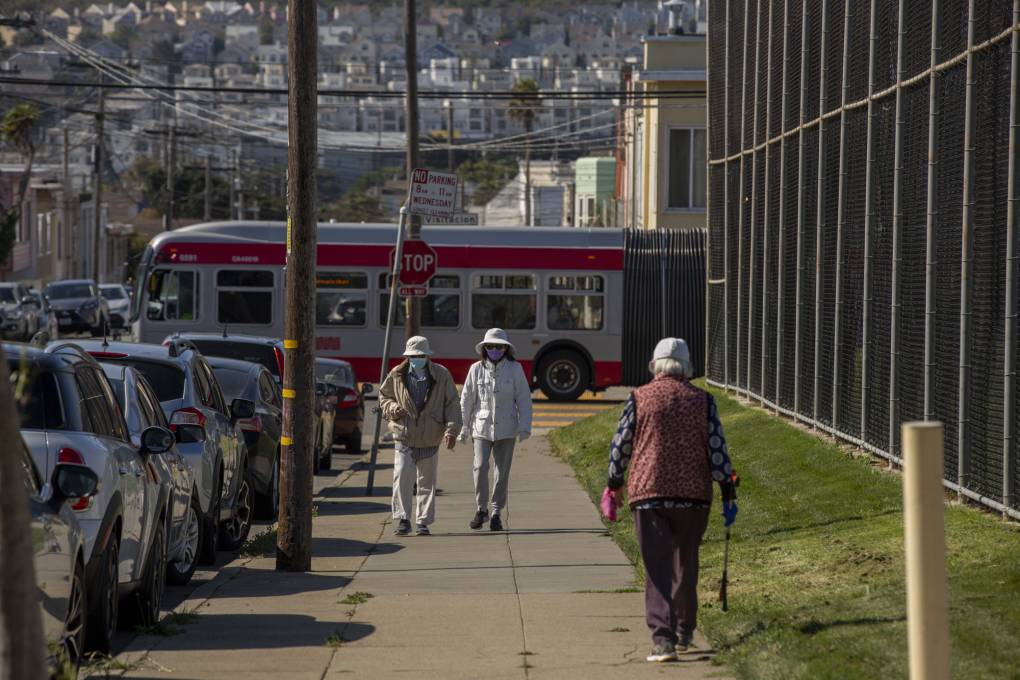 Several people walk up a sidewalk next to a grassy park.