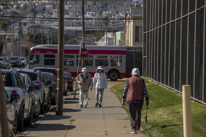 Several people walk up a sidewalk next to a grassy park.