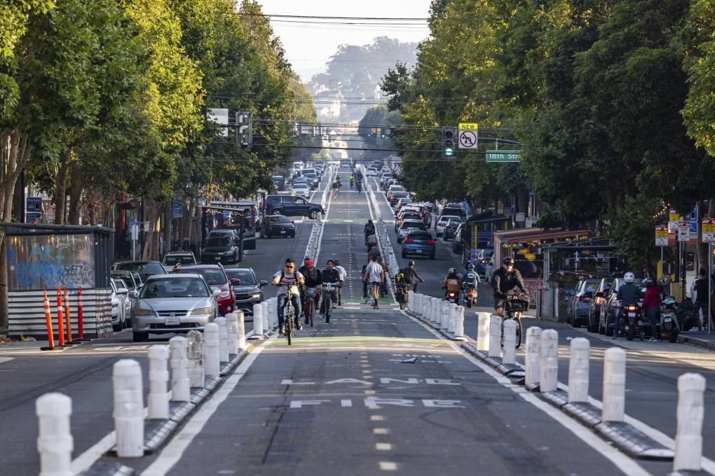 People on bikes and skateboards ride down a bike path in the middle of a city street.