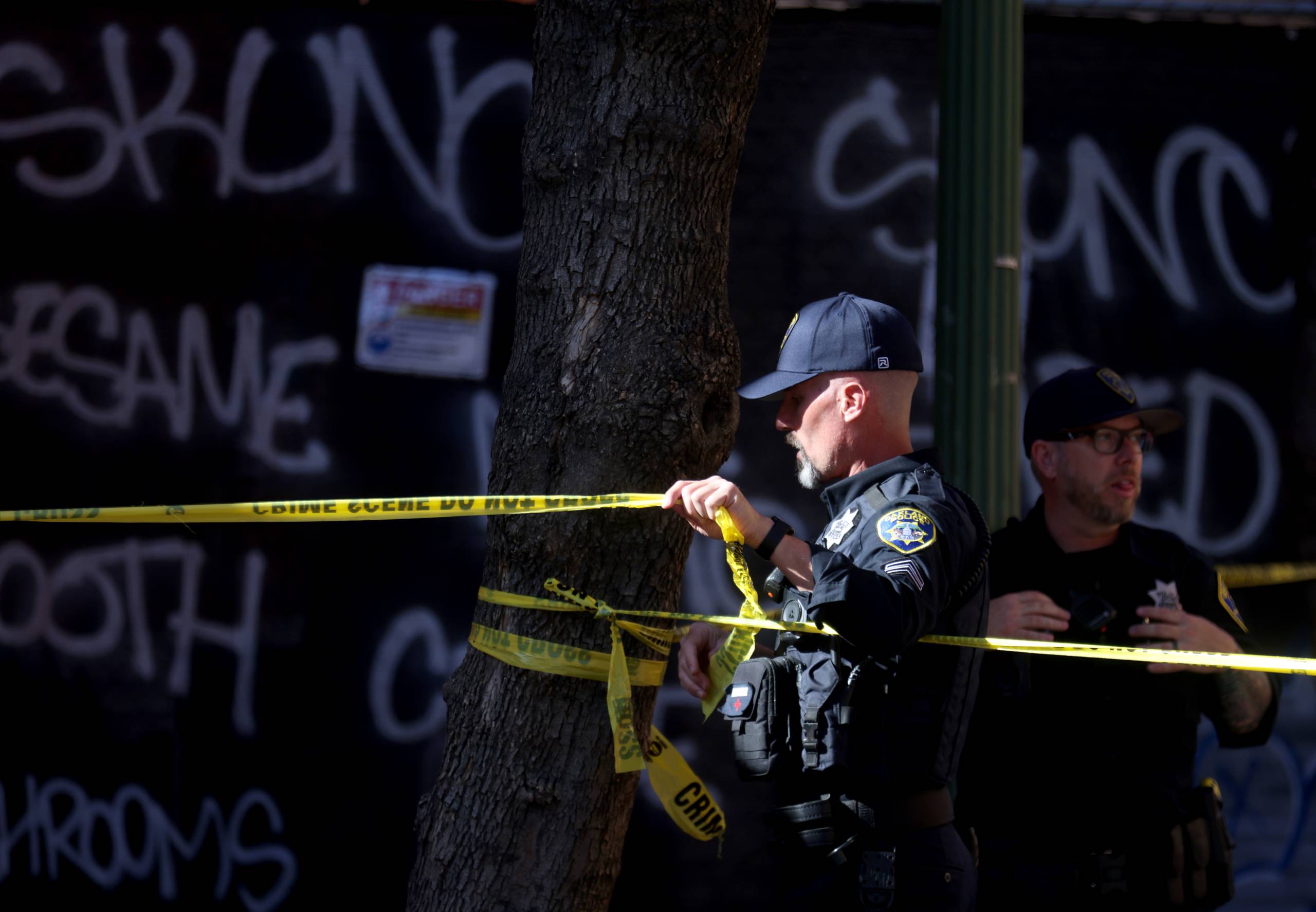 An Oakland police officer puts yellow crime tape around a sidewalk.