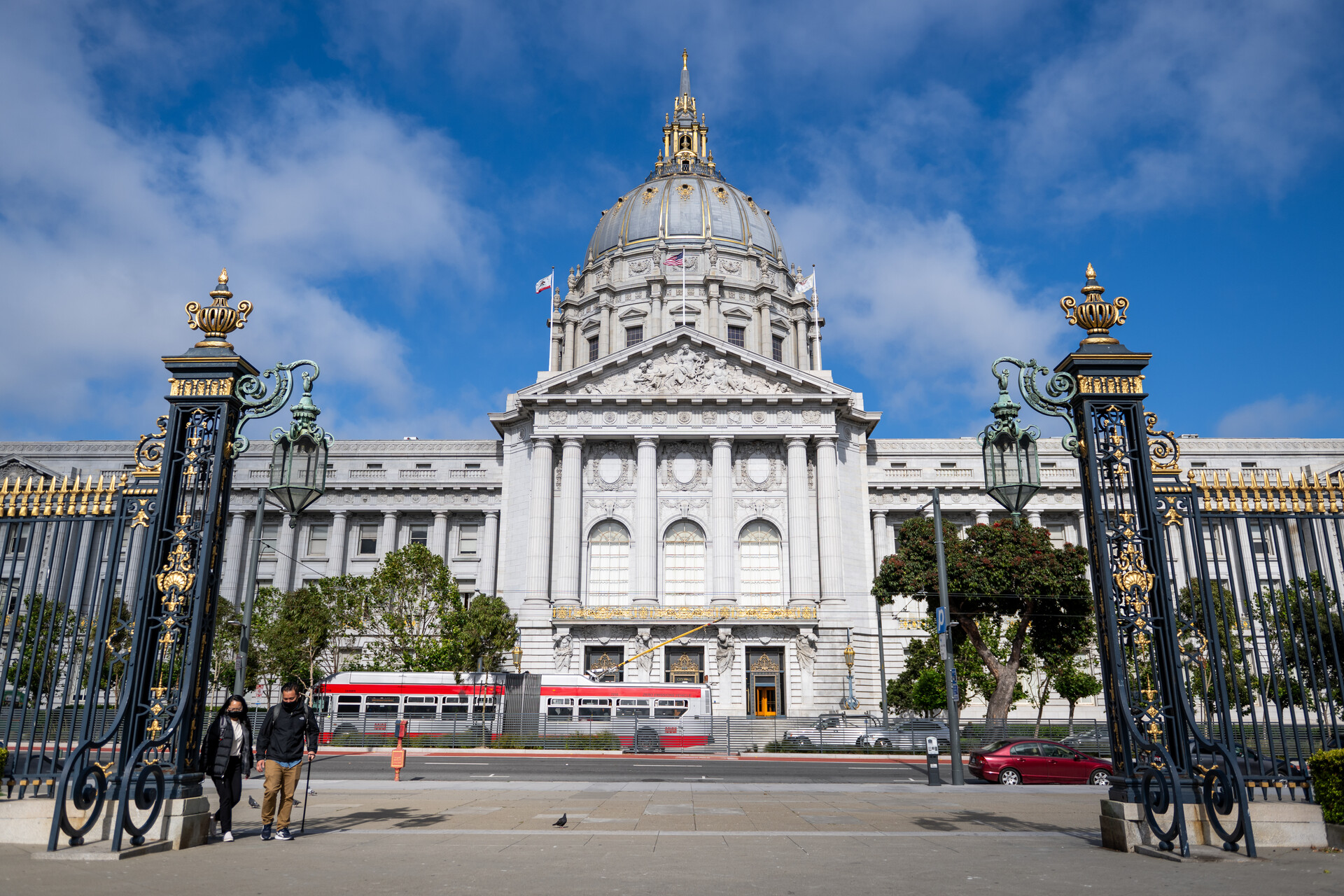 A building with intricate pillars in front, as well as a red and white city bus.