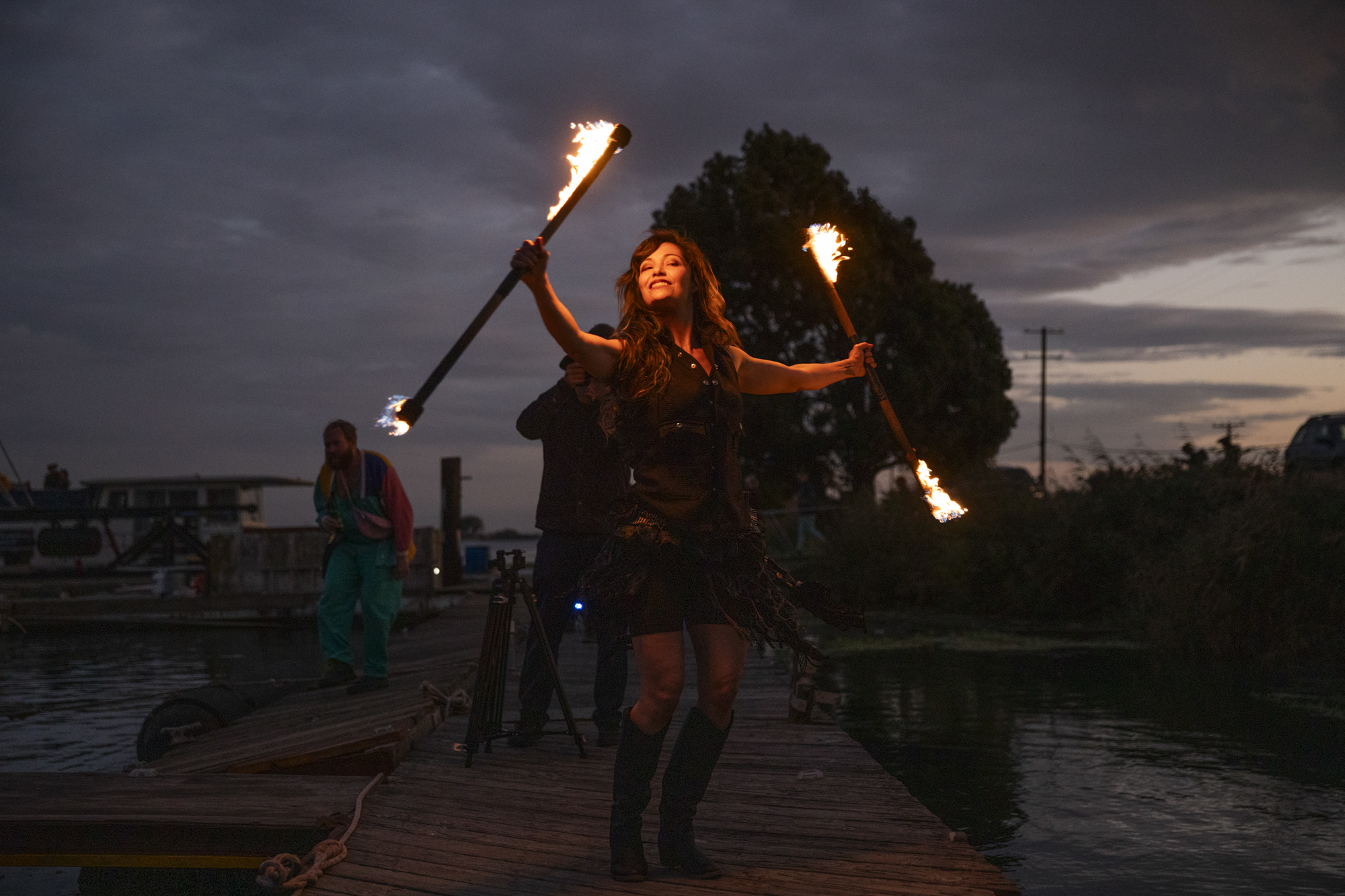 A person smiles and twirls flaming batons.