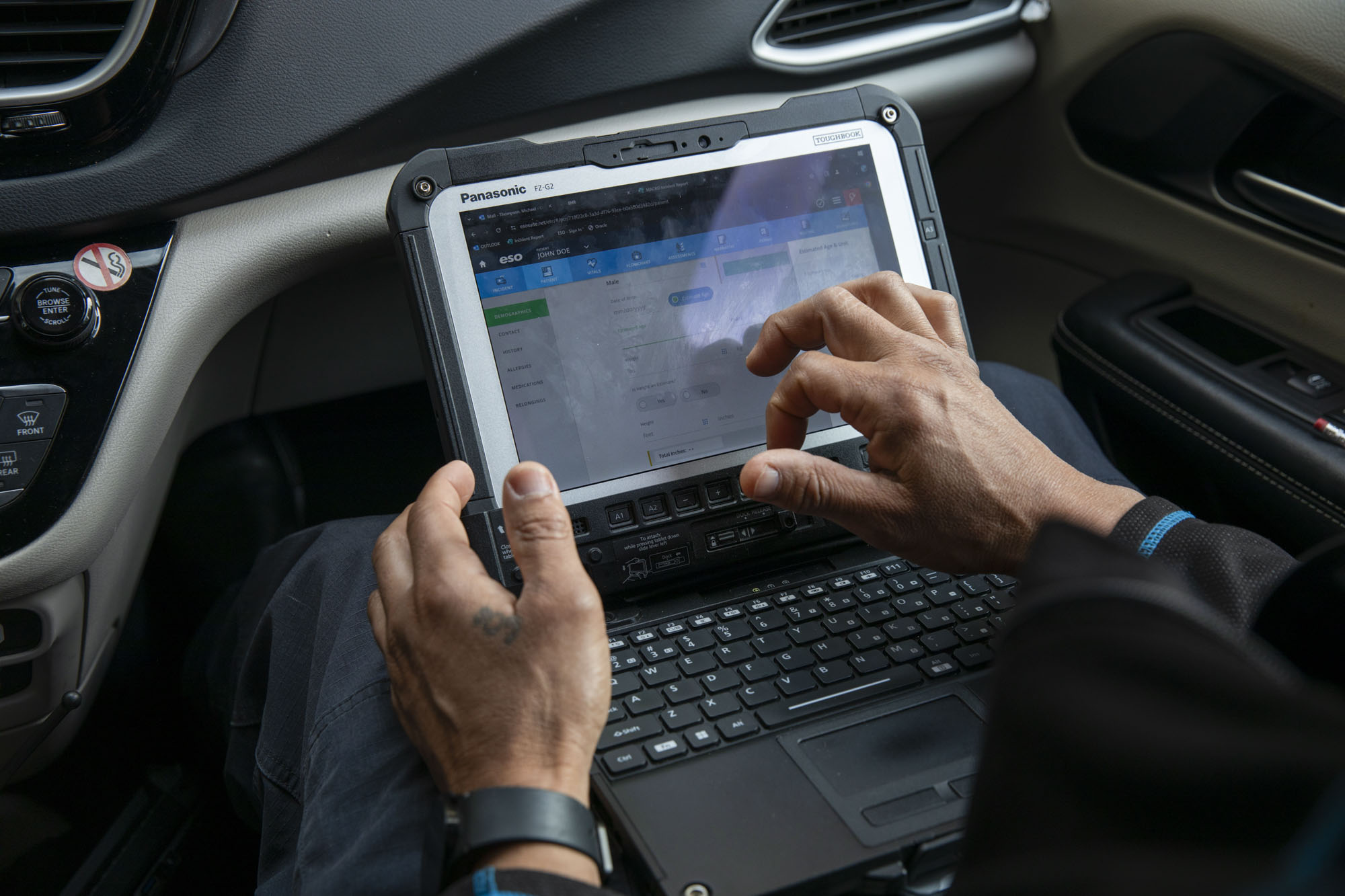 A person types into a laptop from the passenger seat of a car.