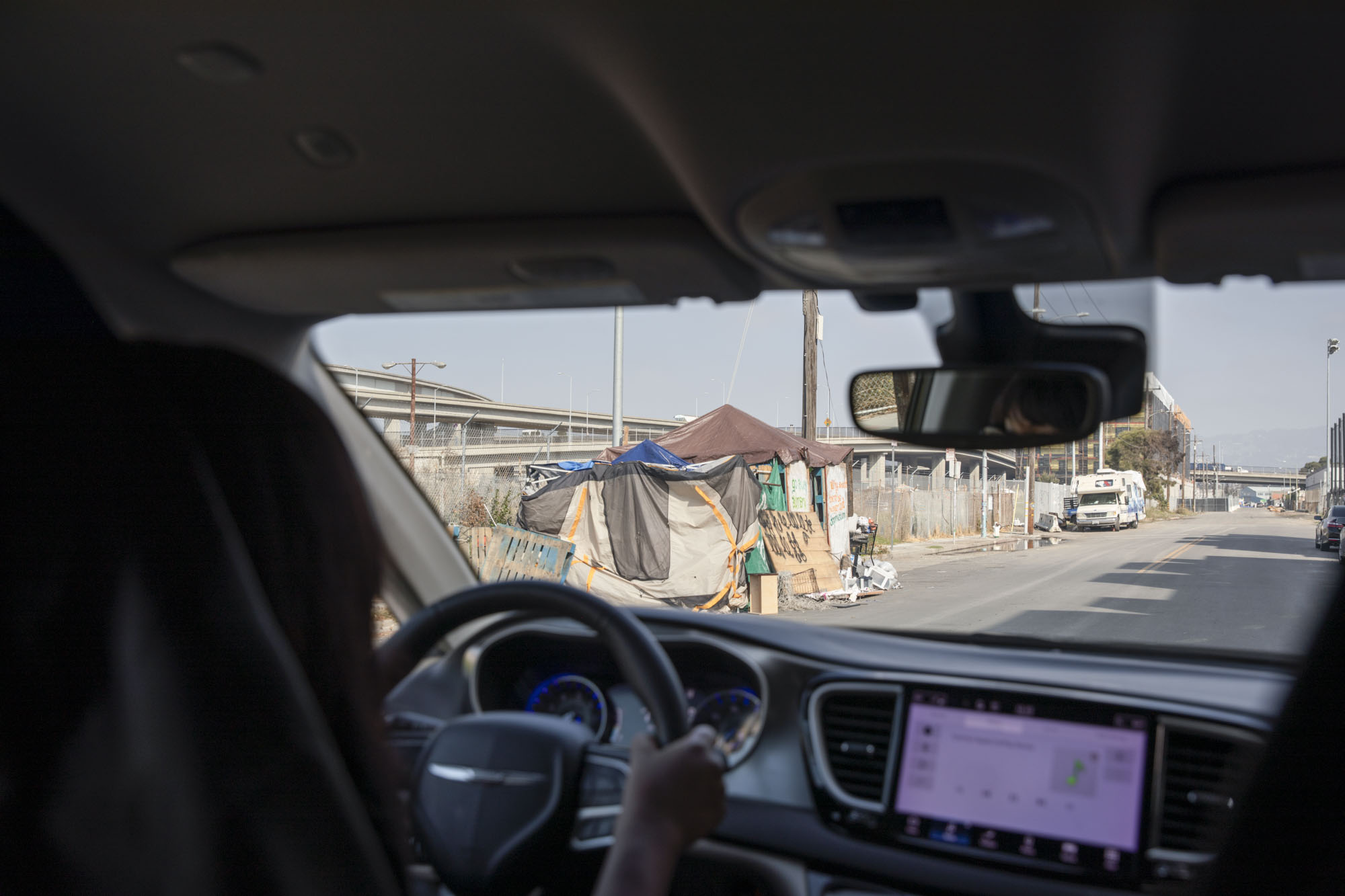 A homeless encampment is seen through the windshield of a car.