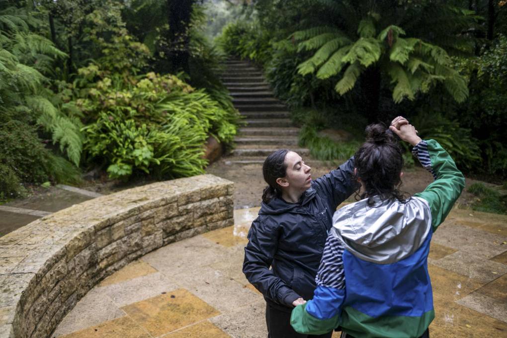 Two people hold each other, appearing to be dancing, in a wooded area.