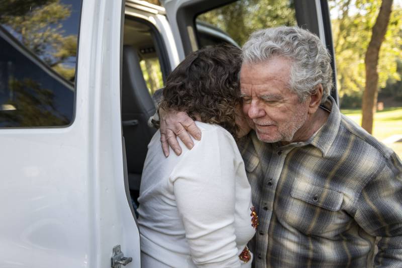 Two people hug beside a vehicle.