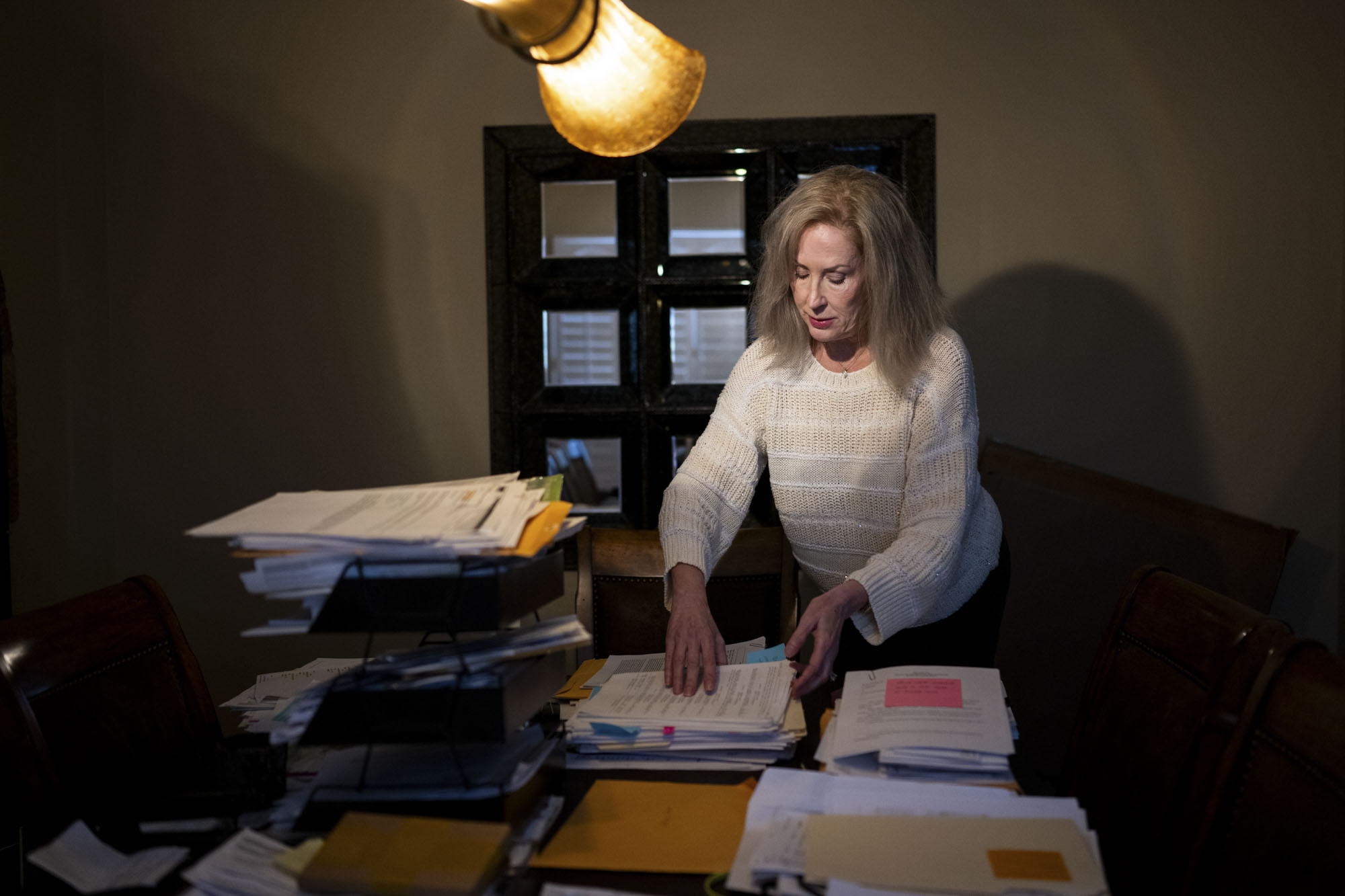 A person with long hair looks through stacks of paperwork.