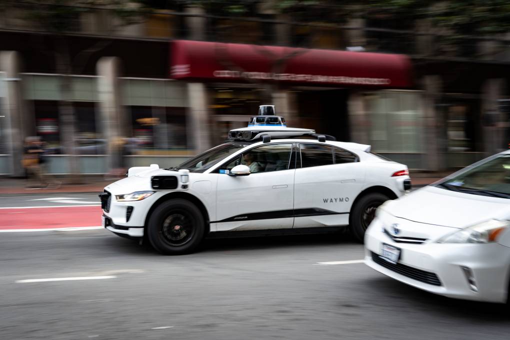 A white driverless vehicle drives on a city street.