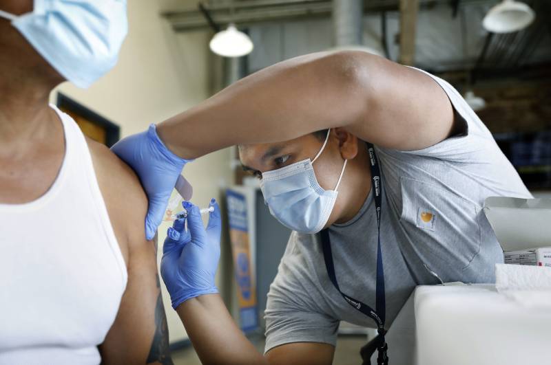 A person wearing a mask and latex gloves administers a shot in another person's arm