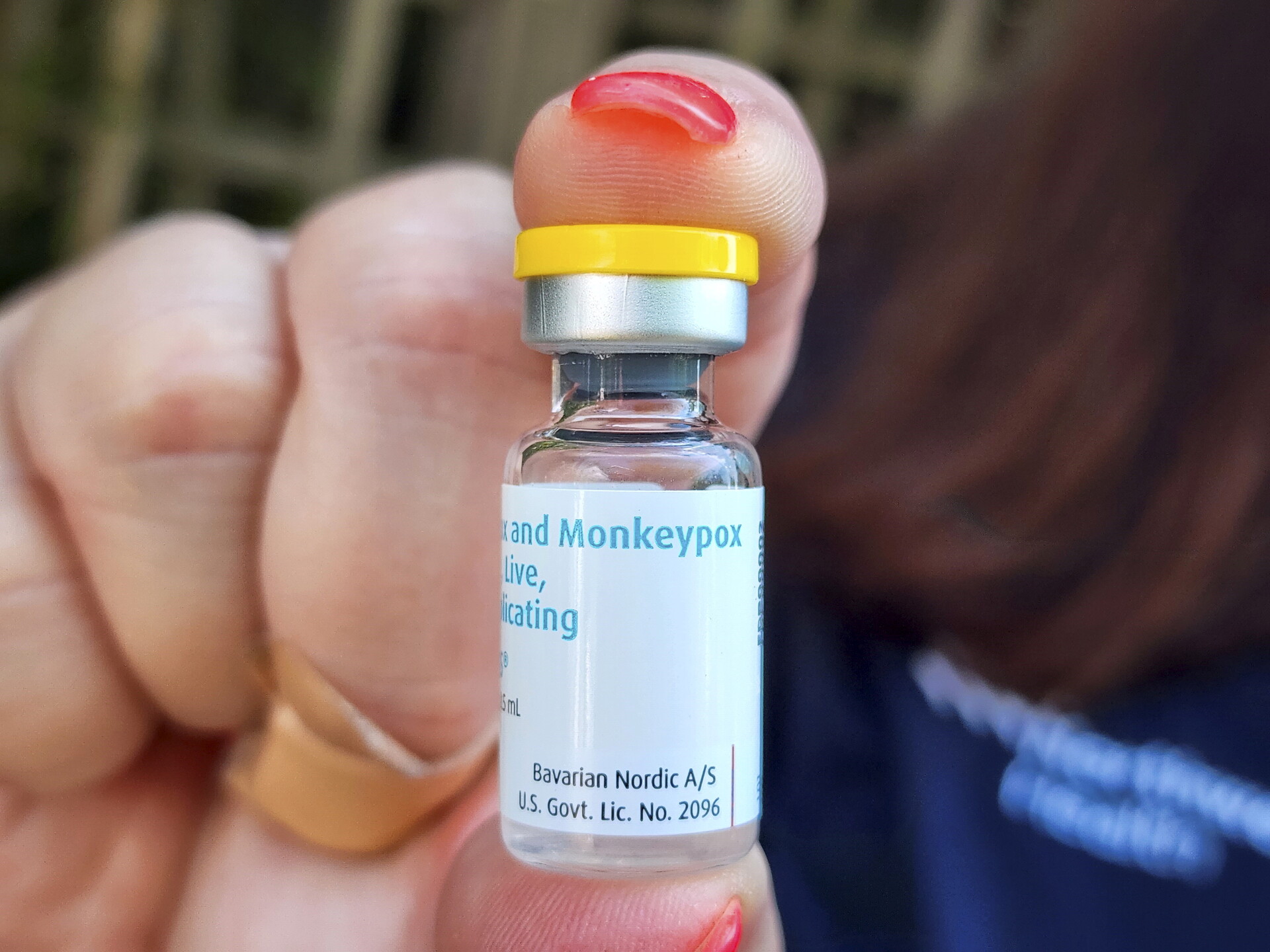 close-up photo of fingers holding a tiny vial which reads 'monkeypox vaccine'