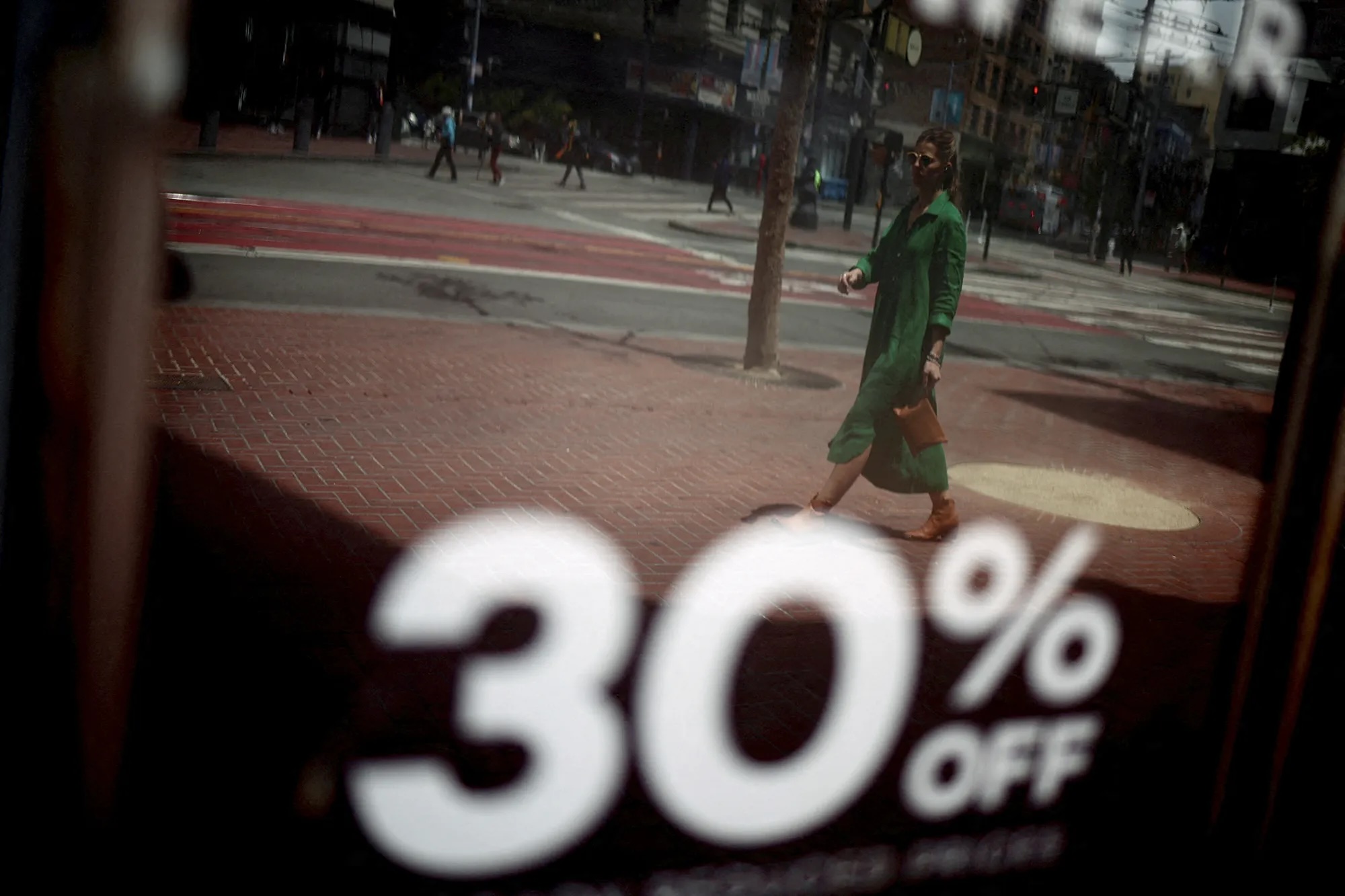 A person walks by a shopfront where "30% Off" is written on the window.